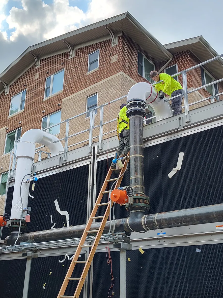 Sabaoth FQ crew fitting an insulated elbow at a rooftop cooling tower beside a brick facade