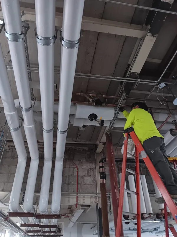 White PVC jacketed piping running overhead while an insulator finishes a valve