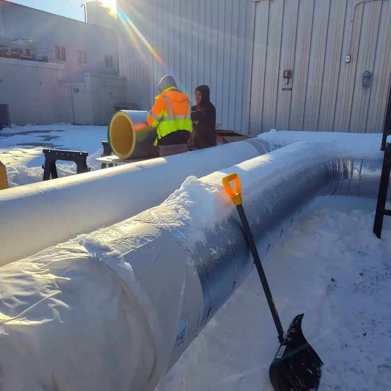 Jacketed ductwork staged on snowy ground while the crew preps insulation