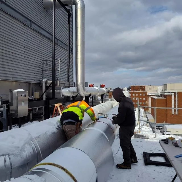 Crew fitting metal jacketing on rooftop piping over snow