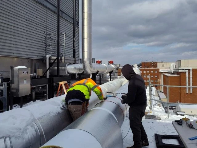 Crew fitting metal jacketing on rooftop piping in the snow